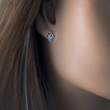 Load image into Gallery viewer, A close-up of a woman's ear wearing a small diamond shaped silver stud earring with a floral design and a red gemstone.
