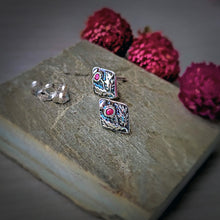 Load image into Gallery viewer, Silver-toned square stud earrings with an oxidized colorful floral detailing and a small pink gemstone, displayed on a textured stone slab with decorative pink flowers in the background.
