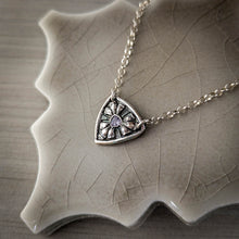 Load image into Gallery viewer, Silver necklace with a shield-shaped pendant with a trillion shaped light blue tanzanite on a ceramic surface
