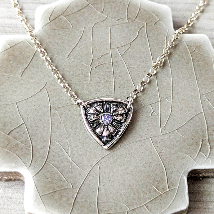 Silver necklace with a shield-shaped pendant with a pale blue tanzanite on a textured surface