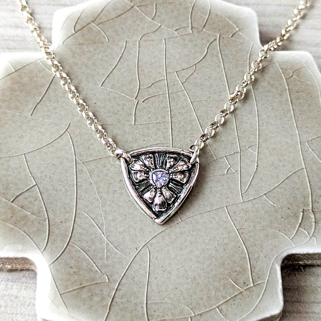 Silver necklace with a shield-shaped pendant with a pale blue tanzanite on a textured surface