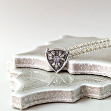 Load image into Gallery viewer, Necklace with a shield-shaped pendant with a light blue tanzanite on a textured stone surface
