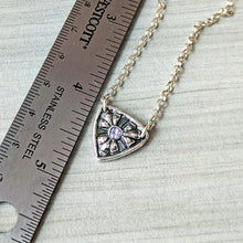 Load image into Gallery viewer, Silver necklace with a shield-shaped pendant next to a ruler for scale
