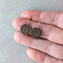 Load image into Gallery viewer, A pair of round, copper toned ornate dangle earrings with intricate circular patterns, held in a person's hand against a neutral gray background.
