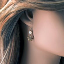 Load image into Gallery viewer, A close-up of a woman's ear wearing a dangling earring with a small white pearl and an antiqued bronze flower charm.
